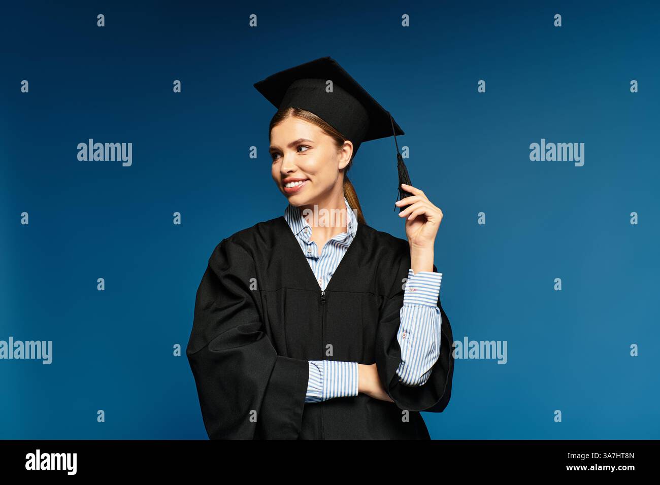 Die junge Frau im Abschlusskleid lächelt selbstbewusst, hält ihre Mütze und freut sich auf neue Abenteuer. Stockfoto