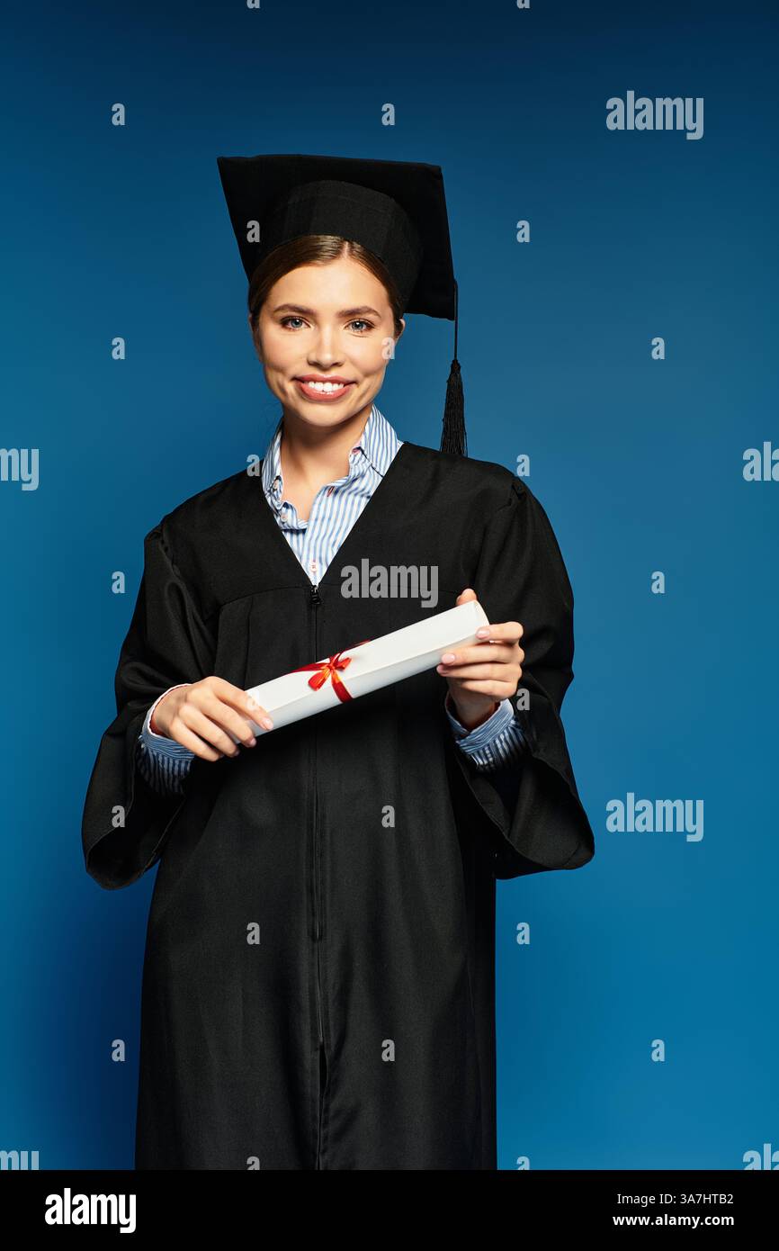 Eine junge Frau im Kleid beamt sich, während sie stolz ihr Diplom mit einem roten Band hält. Stockfoto