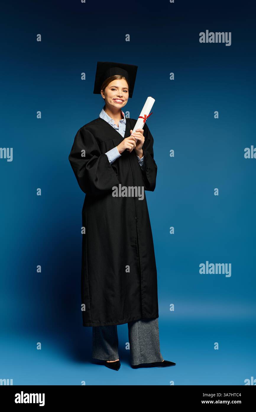 Auf einem hellblauen Hintergrund hält eine fröhliche junge Frau im Abschlussgewand ihr Diplom. Stockfoto