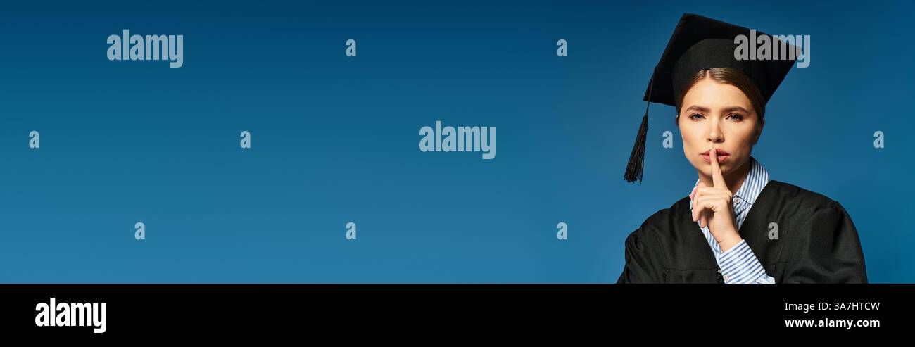 Eine junge Frau im Abschlusskleid signalisiert zum Schweigen, stolz auf ihre akademische Leistung. Stockfoto
