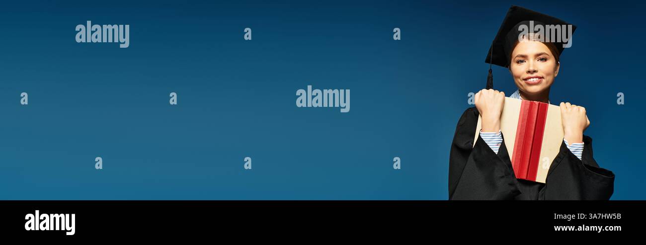 Junge Frau in einer Abschlussmütze posiert mit einem Diplom und lächelt hell vor blauem Hintergrund. Stockfoto
