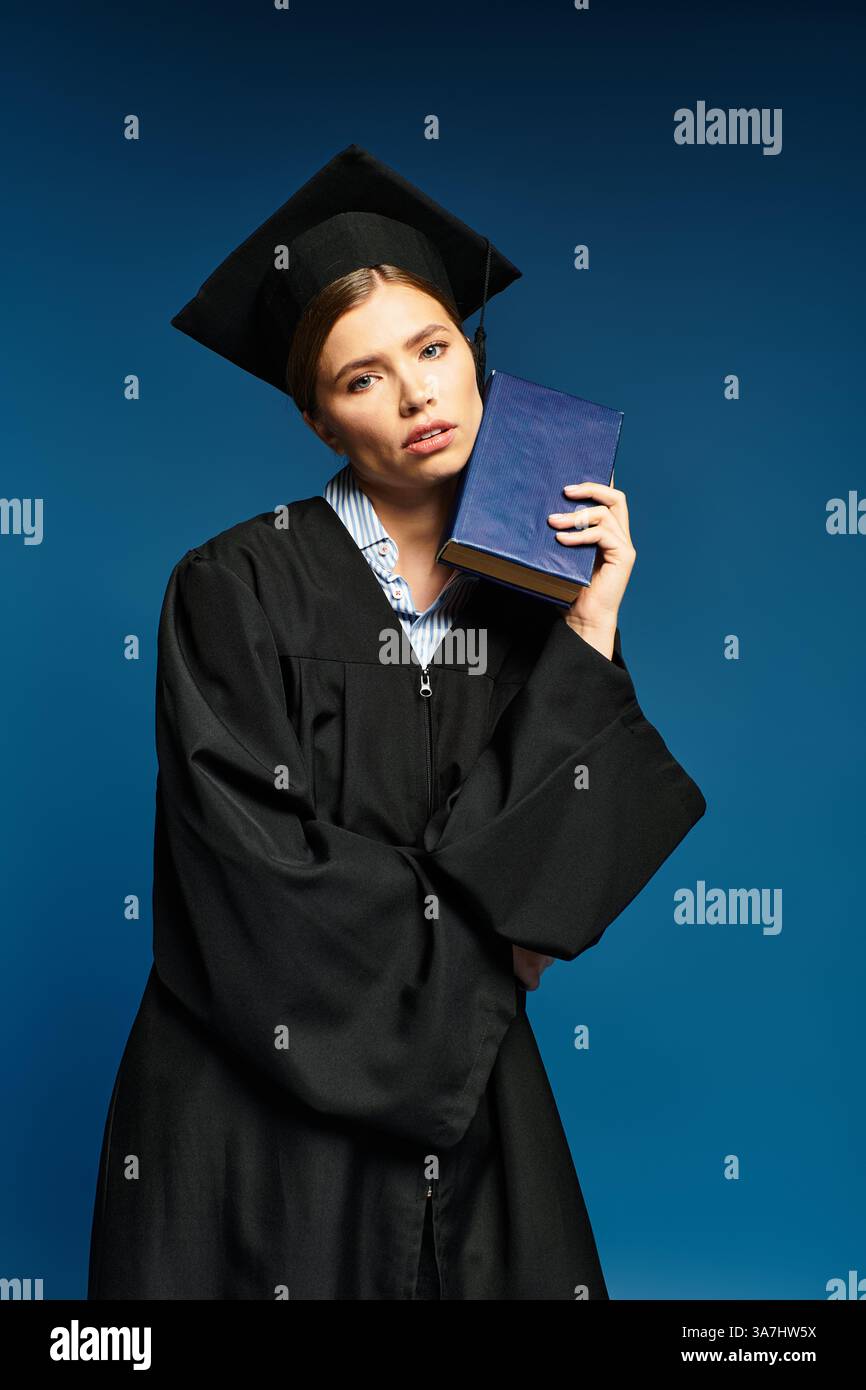 Eine junge Frau in Abschlusskleidung hält ein Buch und strahlt Stolz und Nachsicht aus. Stockfoto