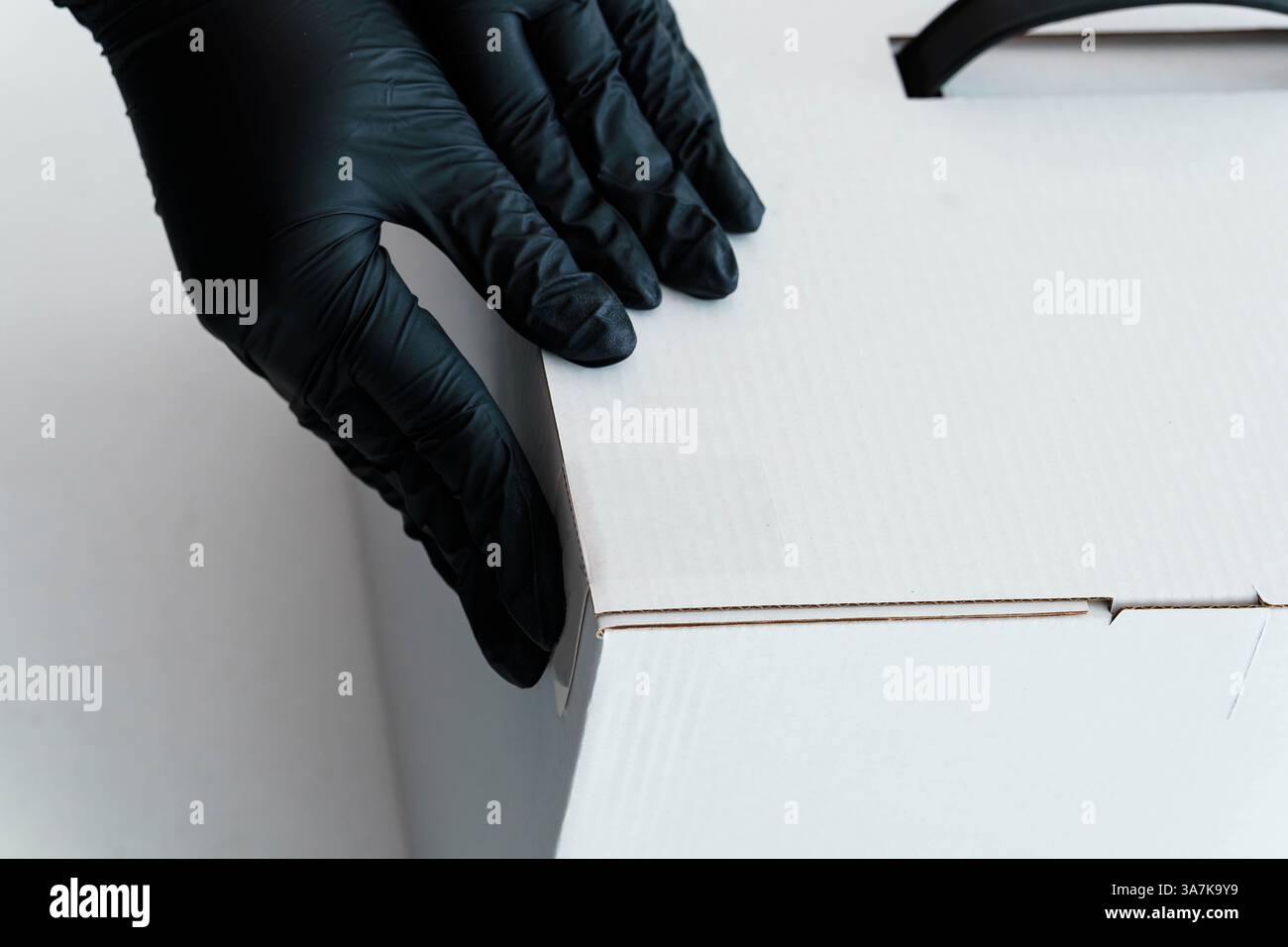 Nahaufnahme der Hände mit schwarzen Handschuhen vorsichtig mit der Verpackung aus weißem Karton. Stockfoto