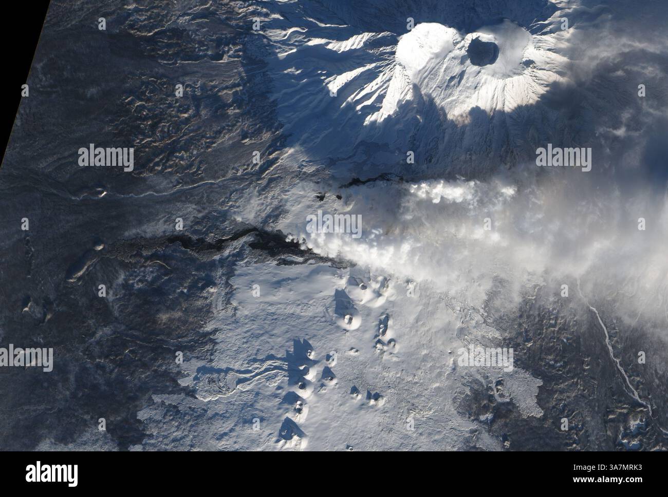22. Dezember 2012 - nach mehr als einem Monat Eruption fließt die Lava weiter aus Tolbatschik, einem von vielen aktiven Vulkanen auf der russischen Kamchatka-Halbinsel. Vulkanausbruch von Tolbatschik, Kamchatka-Halbinsel, Russland - 22. Dezember 2012. Die aktuelle Eruption auf Tolbatschik begann am 27. November 2012. Lava floss bis zu 20 Kilometer aus einer Linie von Spalten an der Südflanke des Vulkans. Seither hat sich ein Teil der Lava so abgekühlt, dass sich Schnee ansammeln kann. Schneebedeckte Lavaflüsse erscheinen auf diesem Satellitenbild grau. Frischere Lava erscheint schwarz. Ein schwaches, oranges Leuchten am Kopf Stockfoto