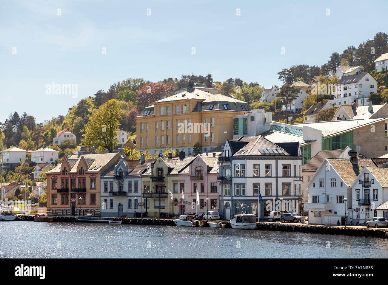An der bezaubernden Uferpromenade in Farsund, Norwegen, finden sich farbenfrohe historische Gebäude am Ufer. Üppiges Grün und blauer Himmel sorgen für die landschaftliche Schönheit Stockfoto