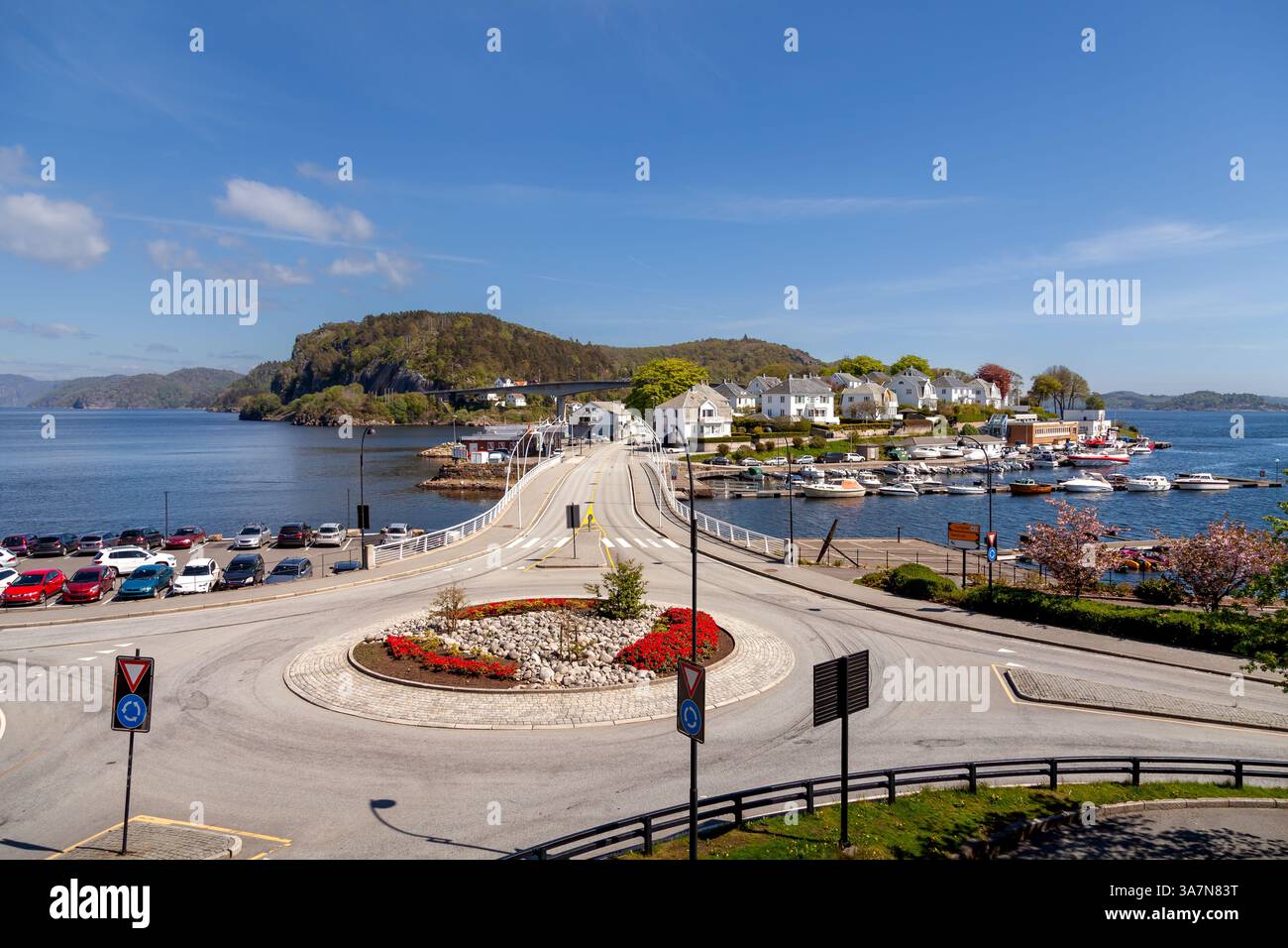 Der Hafen von Farsund bietet eine atemberaubende Aussicht mit Booten, die entlang der Uferpromenade vertäut sind, weißen Häusern auf der Insel Farøy und einer Brücke Stockfoto