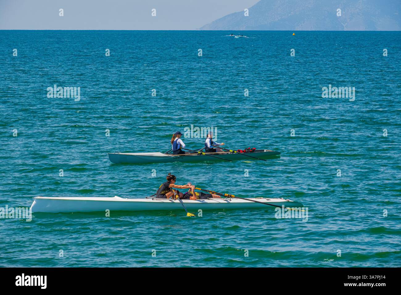 Ruderteams trainieren an einem sonnigen Tag auf offenem Wasser und demonstrieren Teamwork, Ausdauer und Synchronisation im Rudersport. Stockfoto