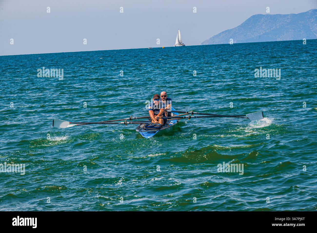 Zwei Individuen rudern ein Doppel-Schädelboot auf dem mäßig abgehackten, sonnendurchfluteten Wasser Stockfoto