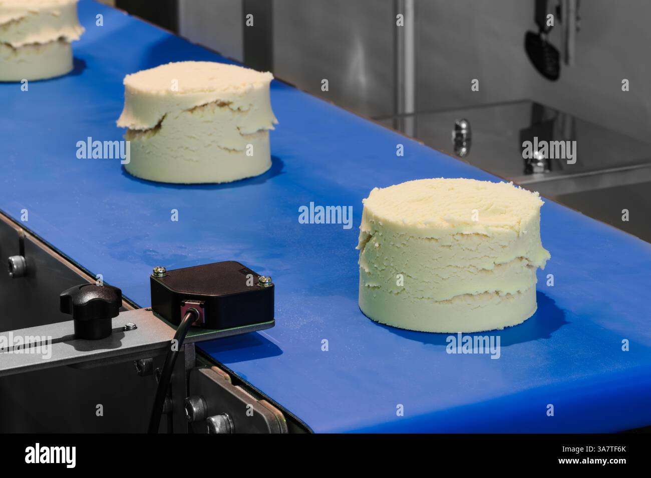 Ein blaues Förderband mit drei Kuchen drauf. Die Kuchen haben alle verschiedene Größen und Formen Stockfoto