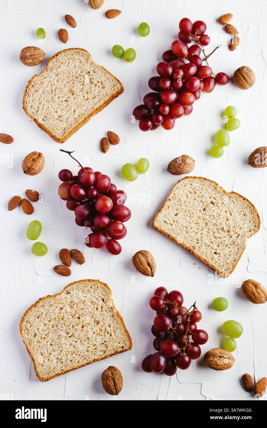 Draufsicht Komposition mit Brotscheiben und rot und grün Trauben auf weißem Tisch mit Walnüssen und Mandeln angeordnet Stockfoto