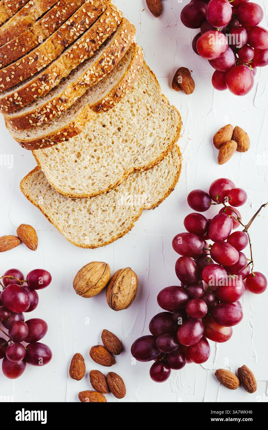 Draufsicht Komposition mit Brotscheiben und rot und grün Trauben auf weißem Tisch mit Walnüssen und Mandeln angeordnet Stockfoto