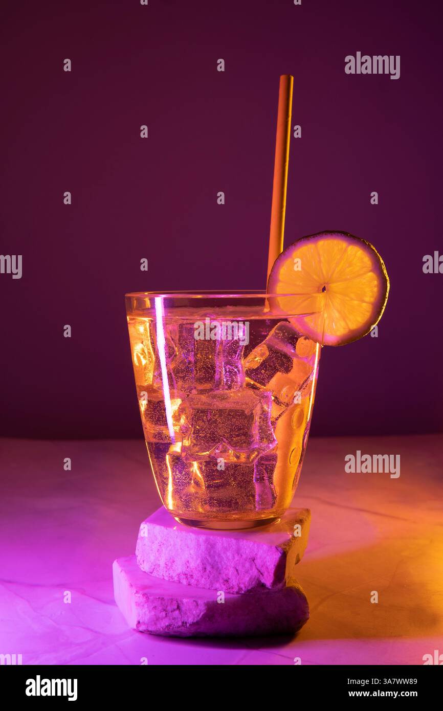 Glas mit Cocktail, Zitrone und farbigen Lichtern Stockfoto
