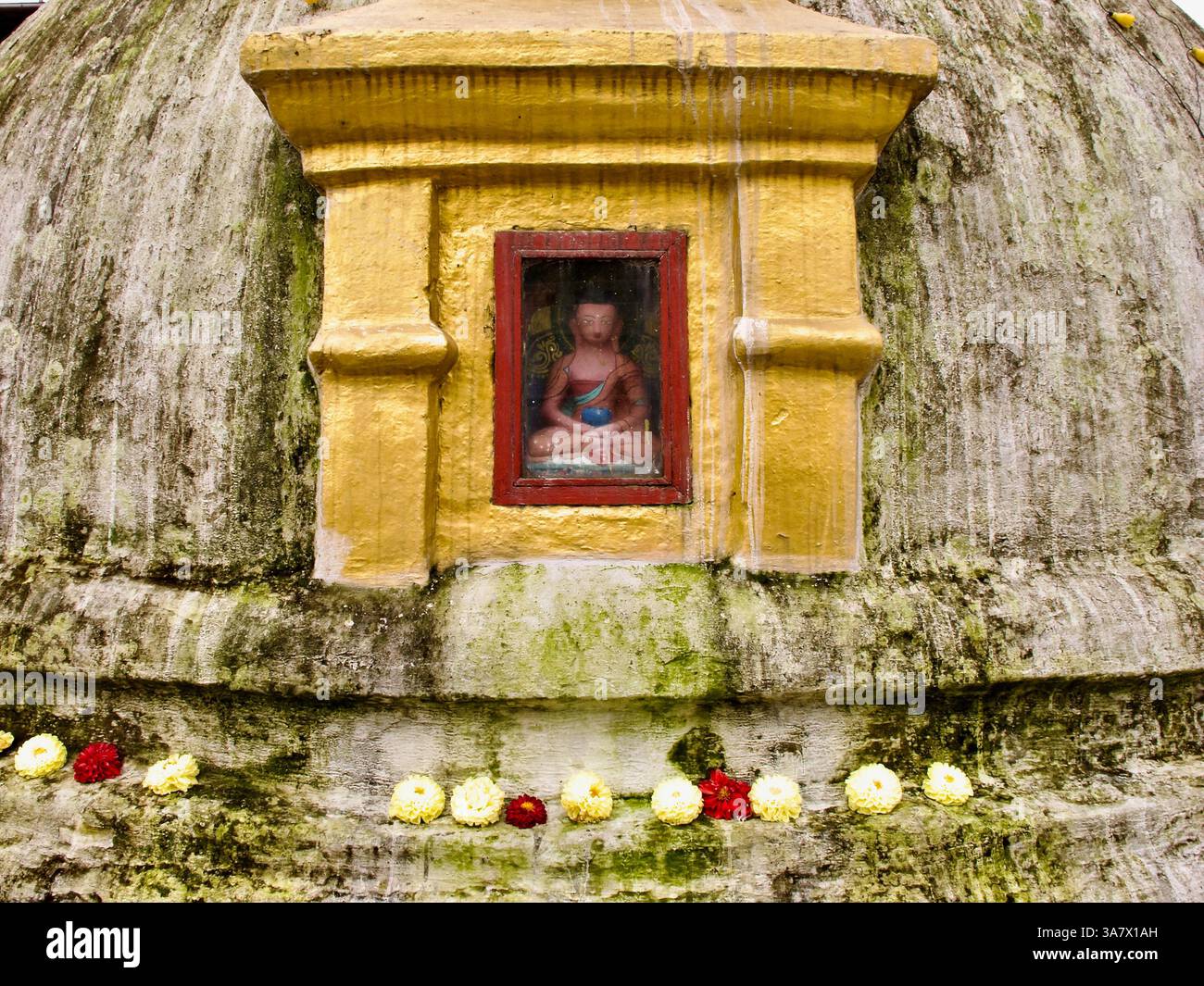 Kleine Buddha-Statue in einer Nische auf der moosgestreiften Kuppel von Boudhanath Stupa, eingerahmt von Ringelblumen- und Chrysanthemen-Opfergaben. Stockfoto