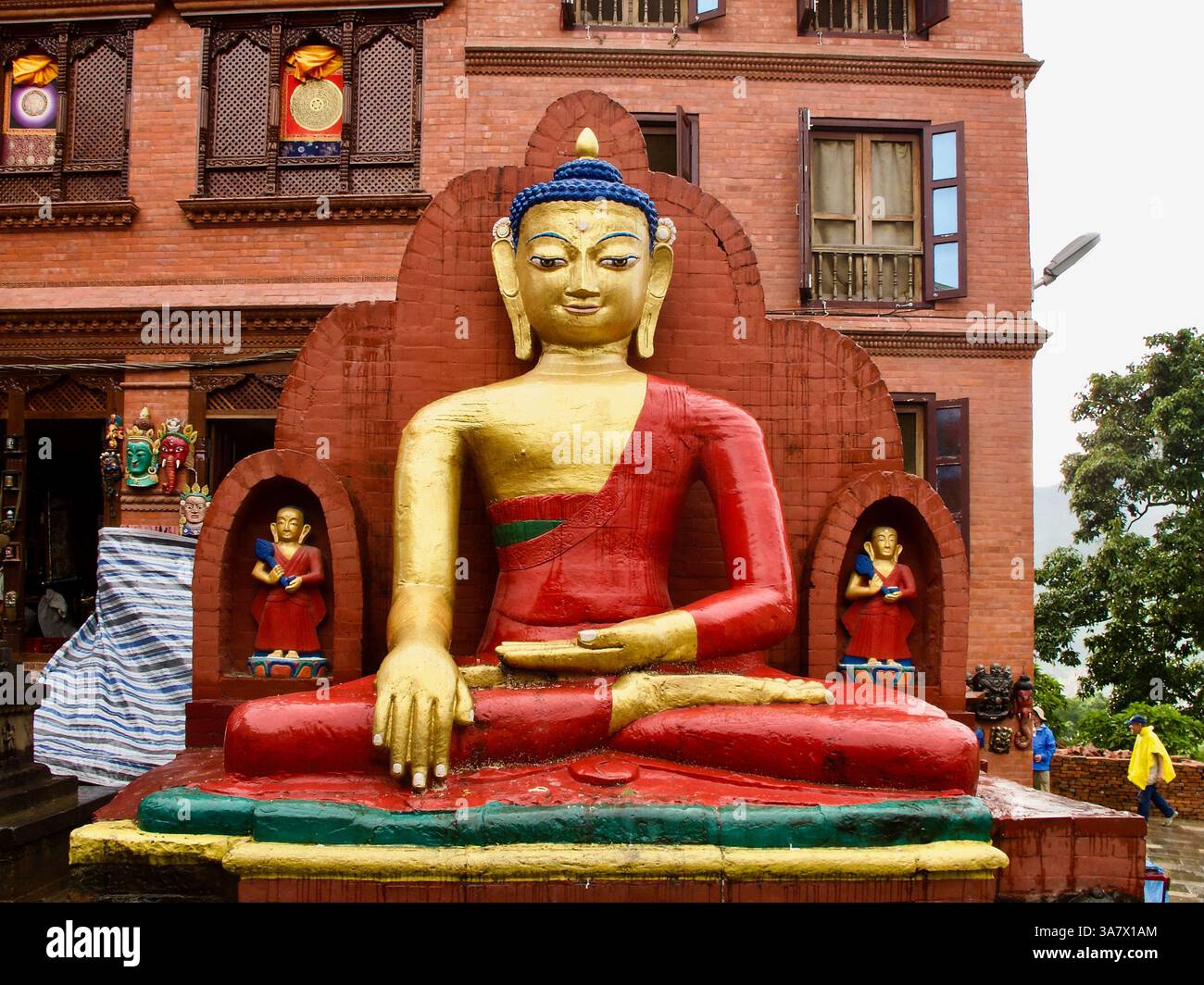 Sitzende Buddha-Statue am östlichen Zugang zu Swayambhunath, Kathmandu, Nepal, flankiert von bemalten klösterlichen Figuren mit heiligen Texten. Stockfoto
