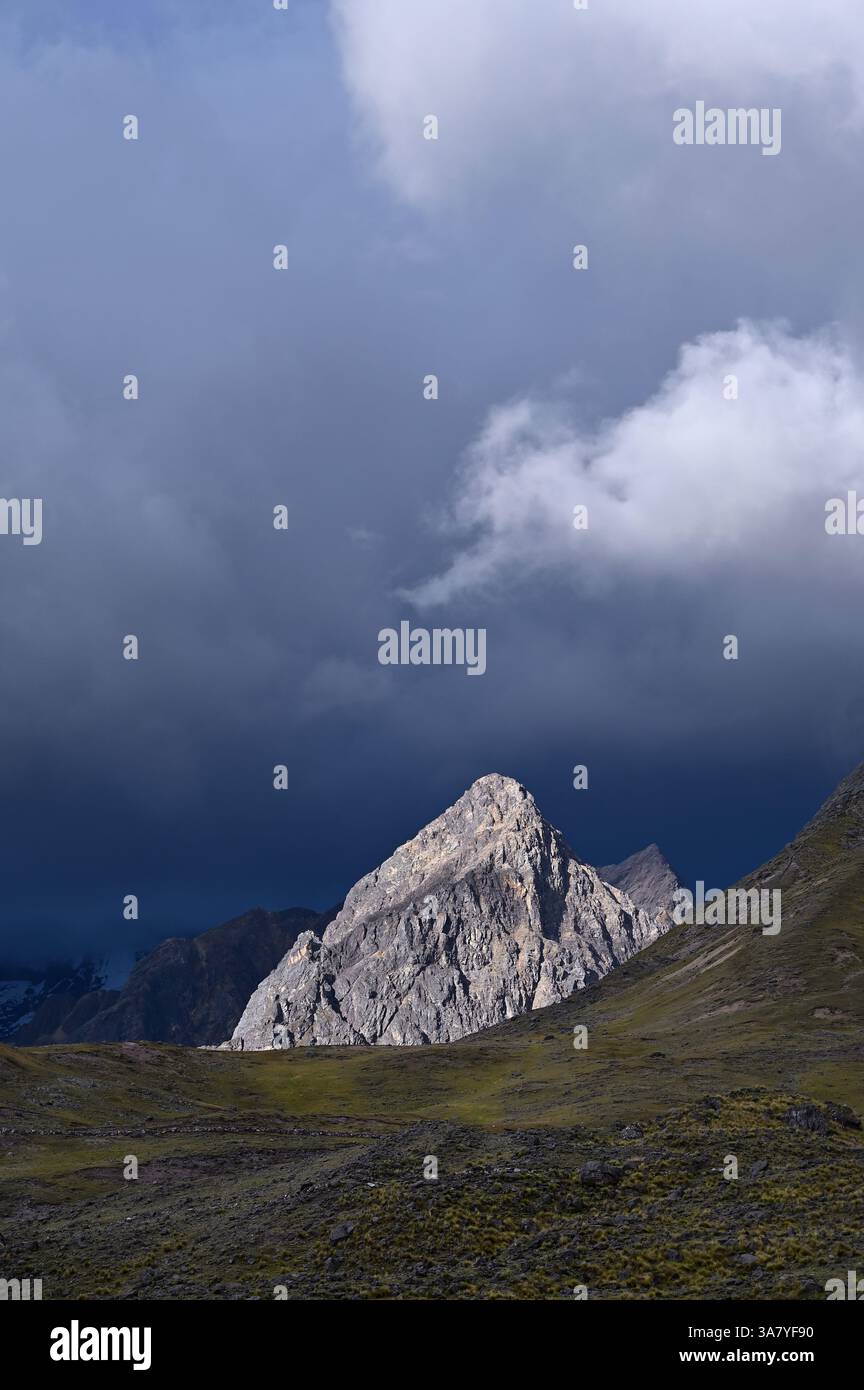Sonnendurchfluteter Berg mit Sturmwolken im Hintergrund. Der Ausangate Berg in der Vilcanota Bergkette. Pacchanta, Cusco, Peru Stockfoto