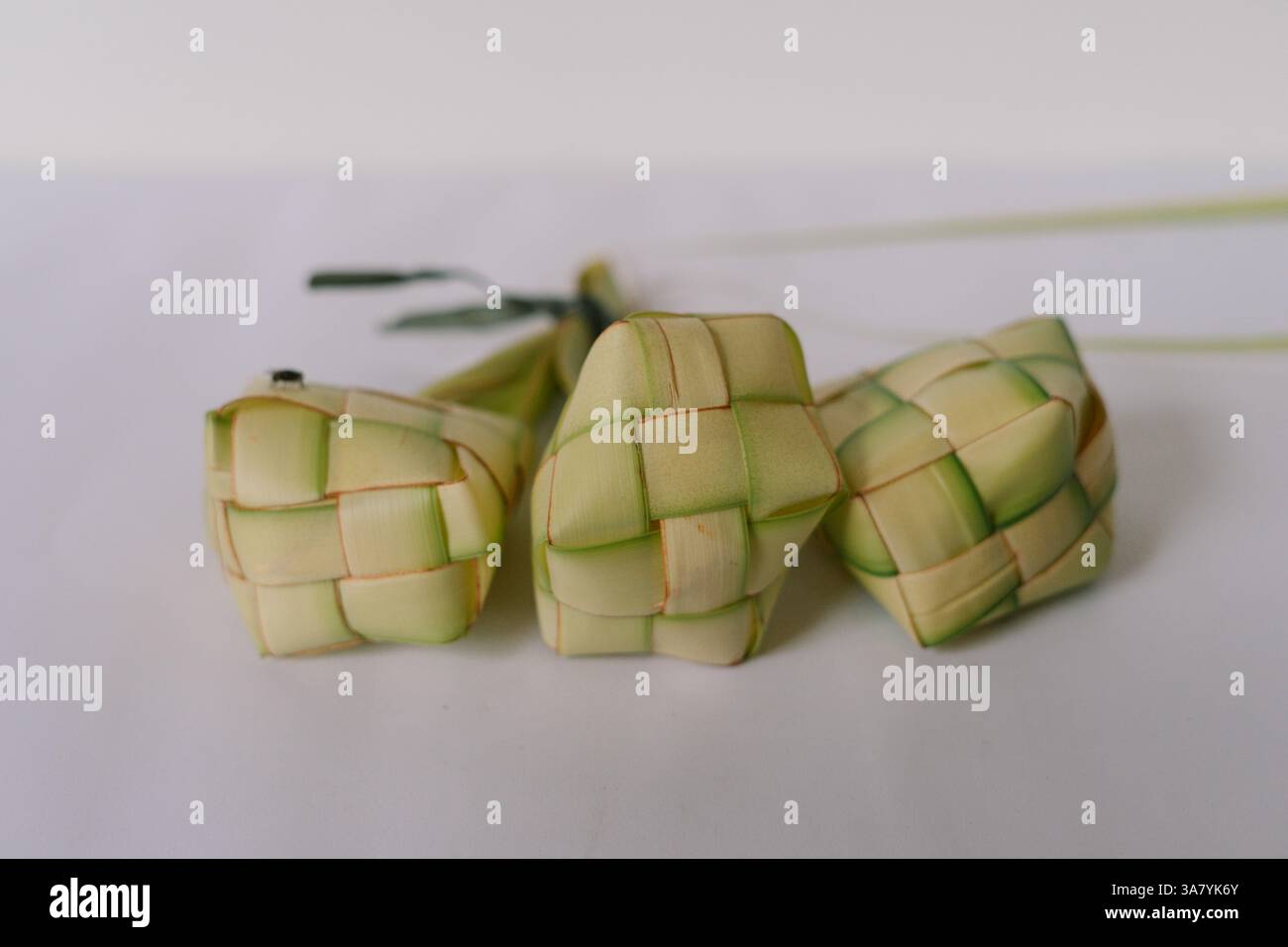 Drei handgewebte Ketupat-Reisknödel werden auf einem schlichten weißen Hintergrund angezeigt. Diese traditionellen malaiischen Köstlichkeiten werden oft während des fes genossen Stockfoto