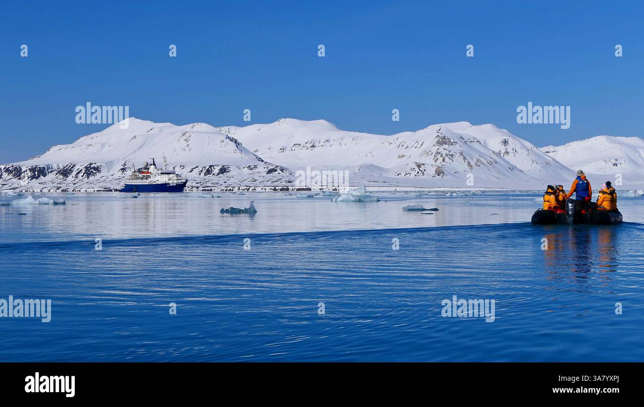 Gruppe unbekannter Reisende in leuchtend orangefarbenen Jacken in einem Zodiac-Boot und Fahrt entlang der ruhigen Wasseroberfläche des Fjords in Svalbard Stockfoto