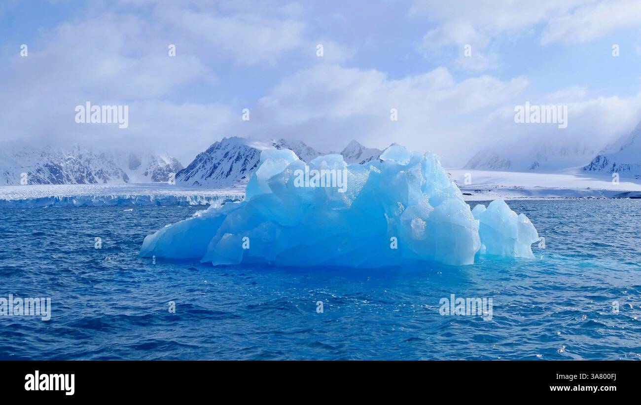 Arktische Landschaft mit blau durchscheinendem Eisberg, der in den eisigen Gewässern eines Fjords im norwegischen Archipel von Svalbard driftet Stockfoto