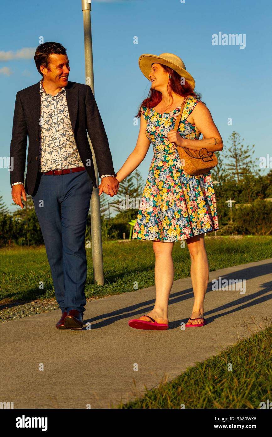 Ein lächelndes Paar genießt einen entspannten Spaziergang im Freien, hält Hände unter dem hellen sonnigen Himmel und zeigt Liebe, Glück und lebhafte Sommermode in A Stockfoto