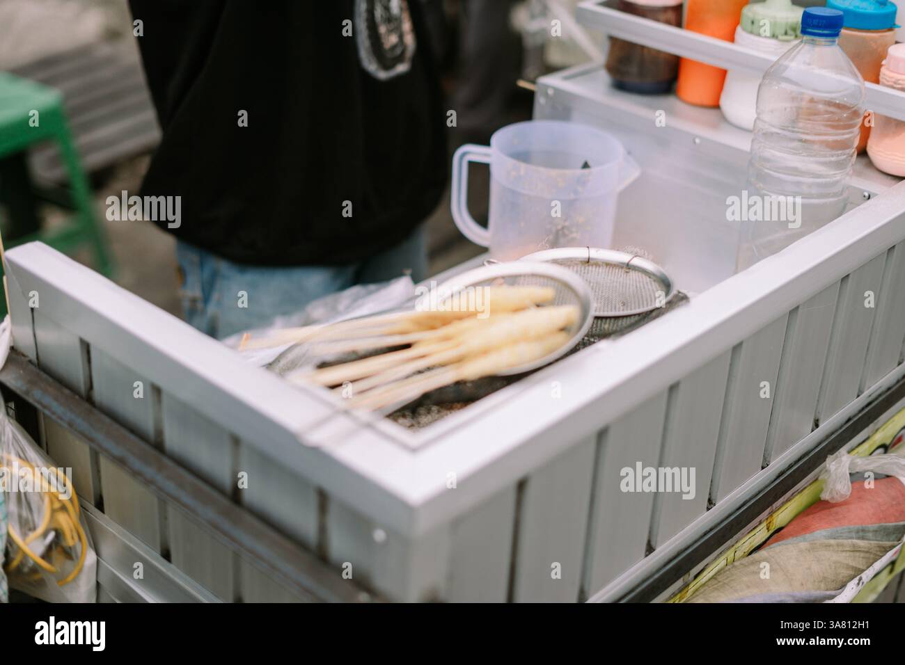 Ein Street Food-Anbieter wird beobachtet, wie er traditionelle Snacks auf einem mobilen Wagen zubereitet. Dies fängt die Essenz der lokalen kulinarischen Kultur und der kleinen Unternehmen ein Stockfoto