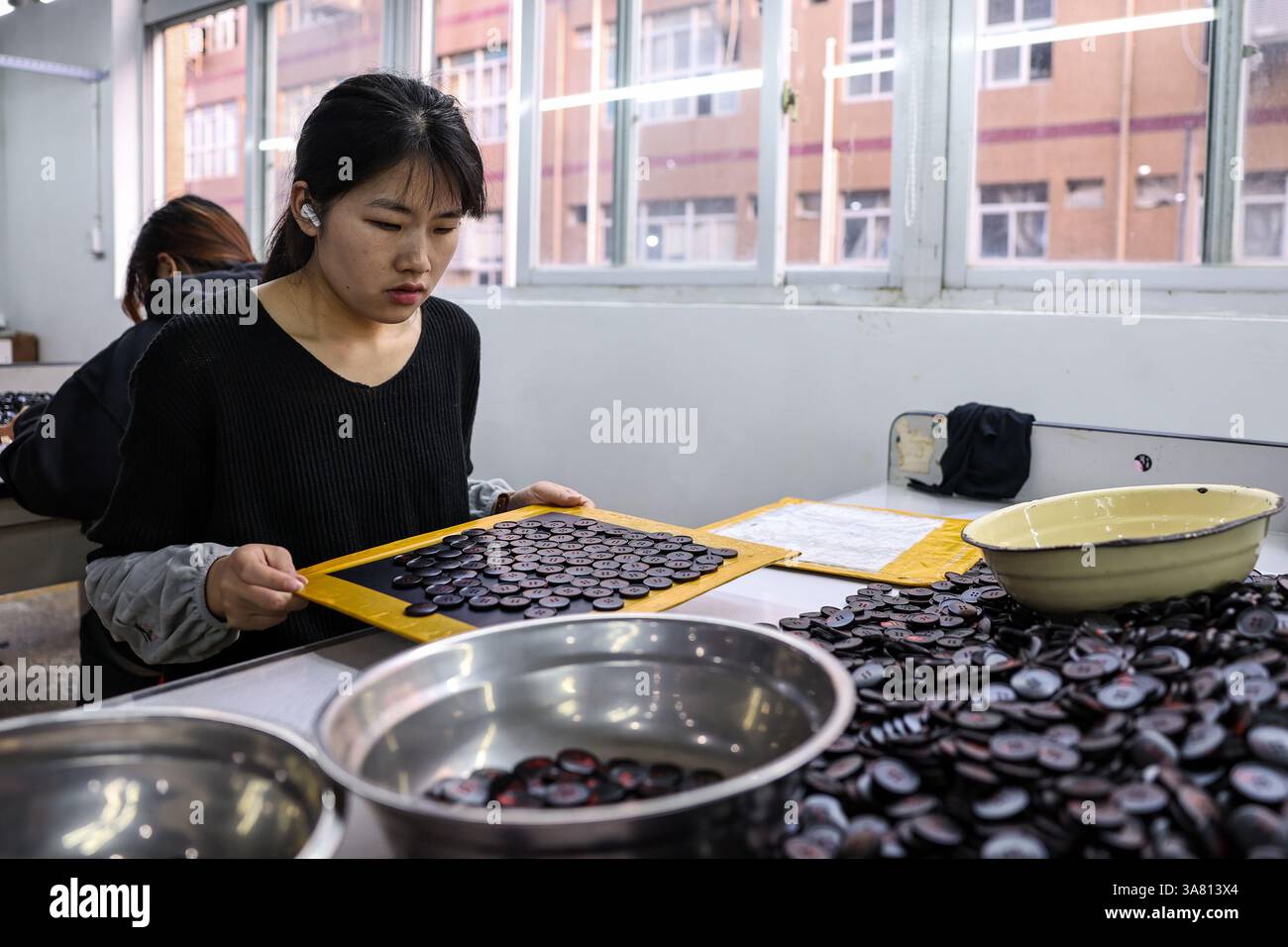 Wenzhou, chinesische Provinz Zhejiang. März 2025. Ein Mitarbeiter arbeitet am 26. März 2025 in einer Werkstatt einer Button-Firma in der Stadt Qiaotou im Kreis Yongjia, Stadt Wenzhou, ostchinesische Provinz Zhejiang. Die Stadt Qiaotou im Yongjia County entwickelt seit Ende der 1970er Jahre ihre Button-Industrie weiter und ist mittlerweile zu einer renommierten „Button Capital“ geworden. Derzeit bieten über 250 Knopfunternehmen im Bezirk Qiaotou Arbeitsplätze für etwa 16.000 Menschen und produzieren rund 60 Milliarden Buttons mit einem Jahresumsatz von über 4 Milliarden Yuan (etwa 550,6 Millionen US-Dollar). Quelle: Jiang Han/Xinhua/Alamy Live News Stockfoto