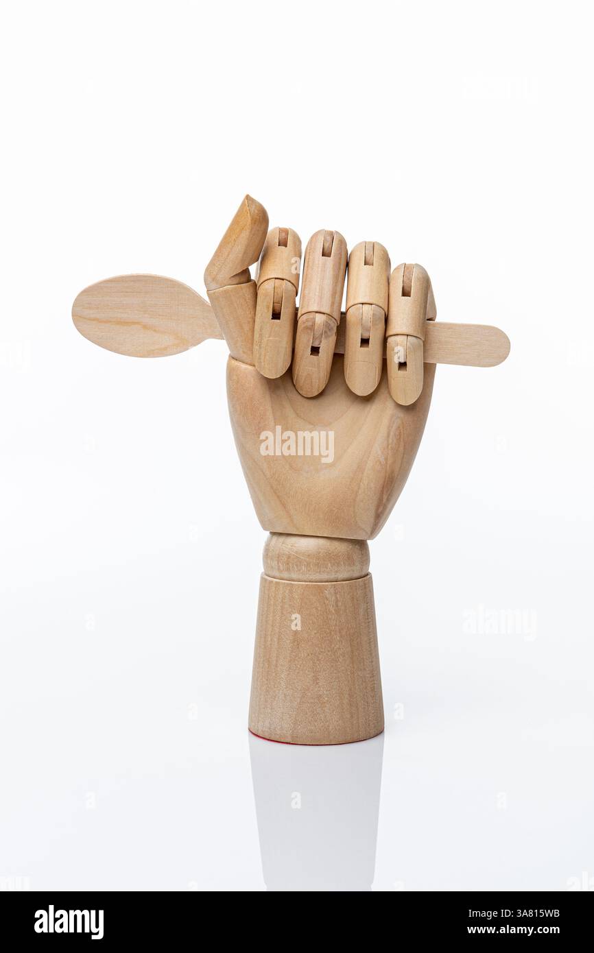 Hölzerner Einweglöffel in einer hölzernen Hand einer Schaufensterpuppe auf weißem Hintergrund. Gesundes Lebensmittelkonzept und Naturproduktkonzept Stockfoto