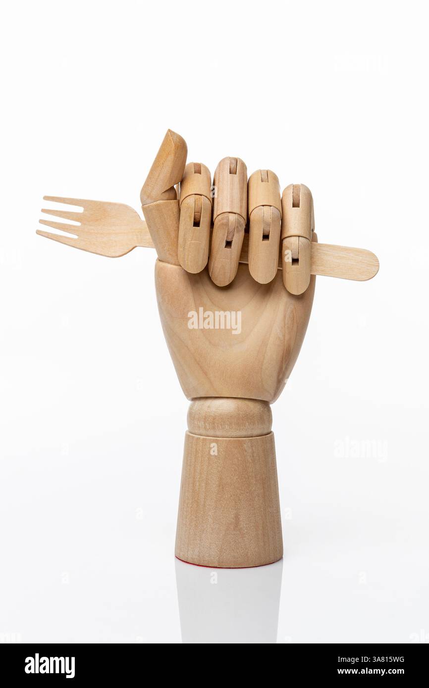 Hölzerne Einweggabel in einer hölzernen Hand einer Schaufensterpuppe auf weißem Hintergrund. Gesundes Lebensmittelkonzept und Naturproduktkonzept Stockfoto