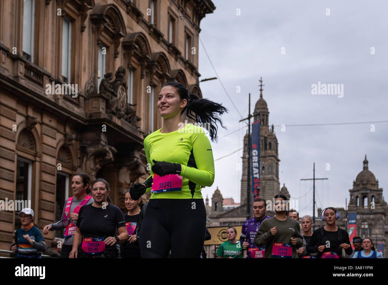Der selbstbewusste Läufer in Neongelb führt eine konzentrierte Gruppe von Teilnehmern während des Great Scottish Run 2024 durch Glasgows Stadtzentrum Stockfoto