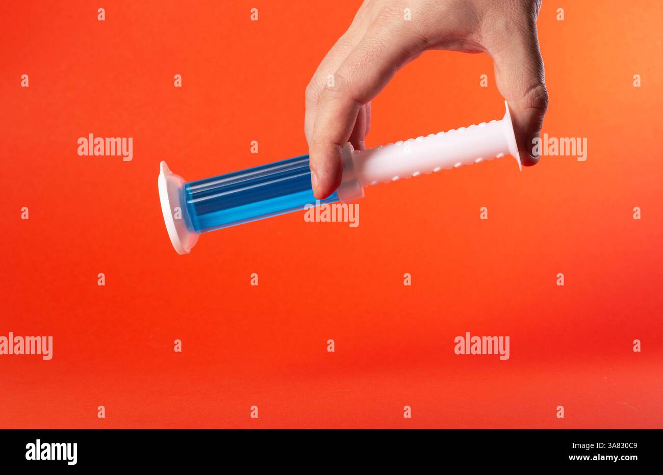 Hand hält eine blaue Spritze mit Toilettenschüsselreiniger auf rotem Hintergrund. Kopierbereich für Text Stockfoto