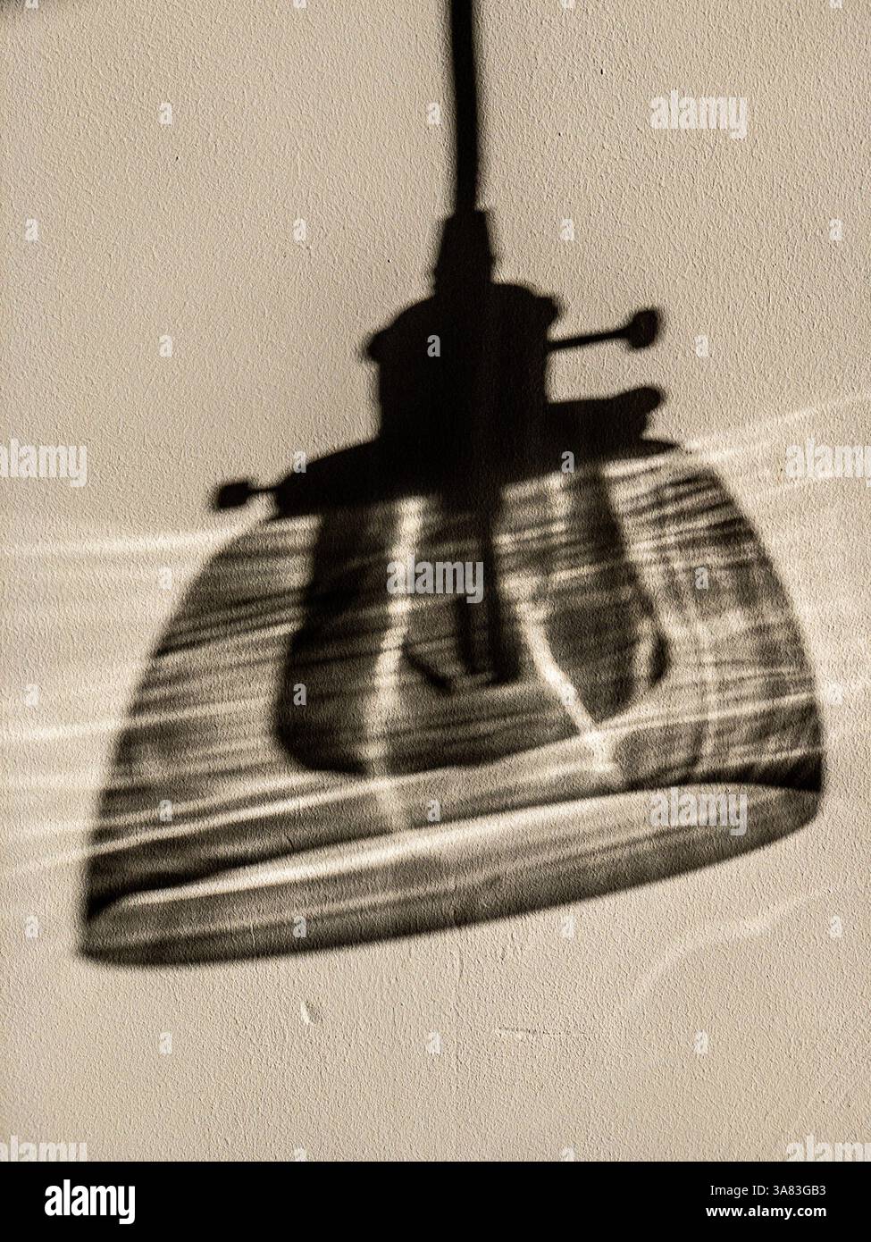 Schatten einer Pendelleuchte mit einem auf eine weiße Wand gegossenen Glasschirm, der ein weiches, anthrazitartiges Bild erzeugt. Stockfoto