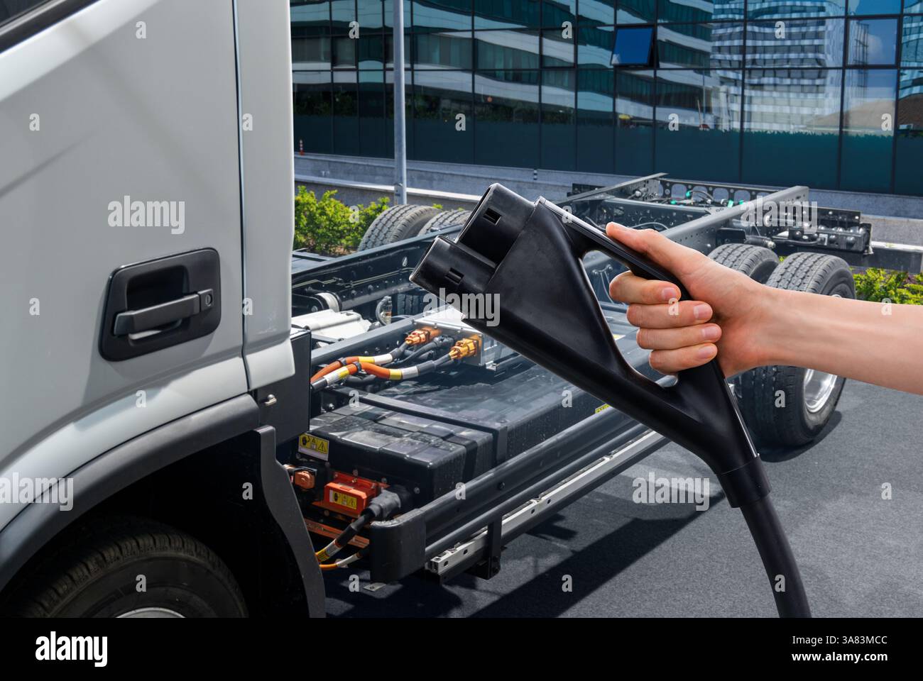 Hand mit Ladestecker auf einem Hintergrund eines Elektrofahrzeugs. Stockfoto