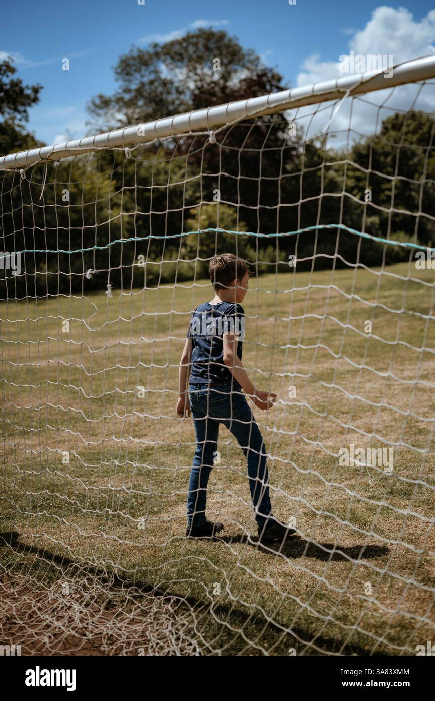 Ein Junge steht vor einem Fußballtor. Ein Blick durch das Netz Stockfoto