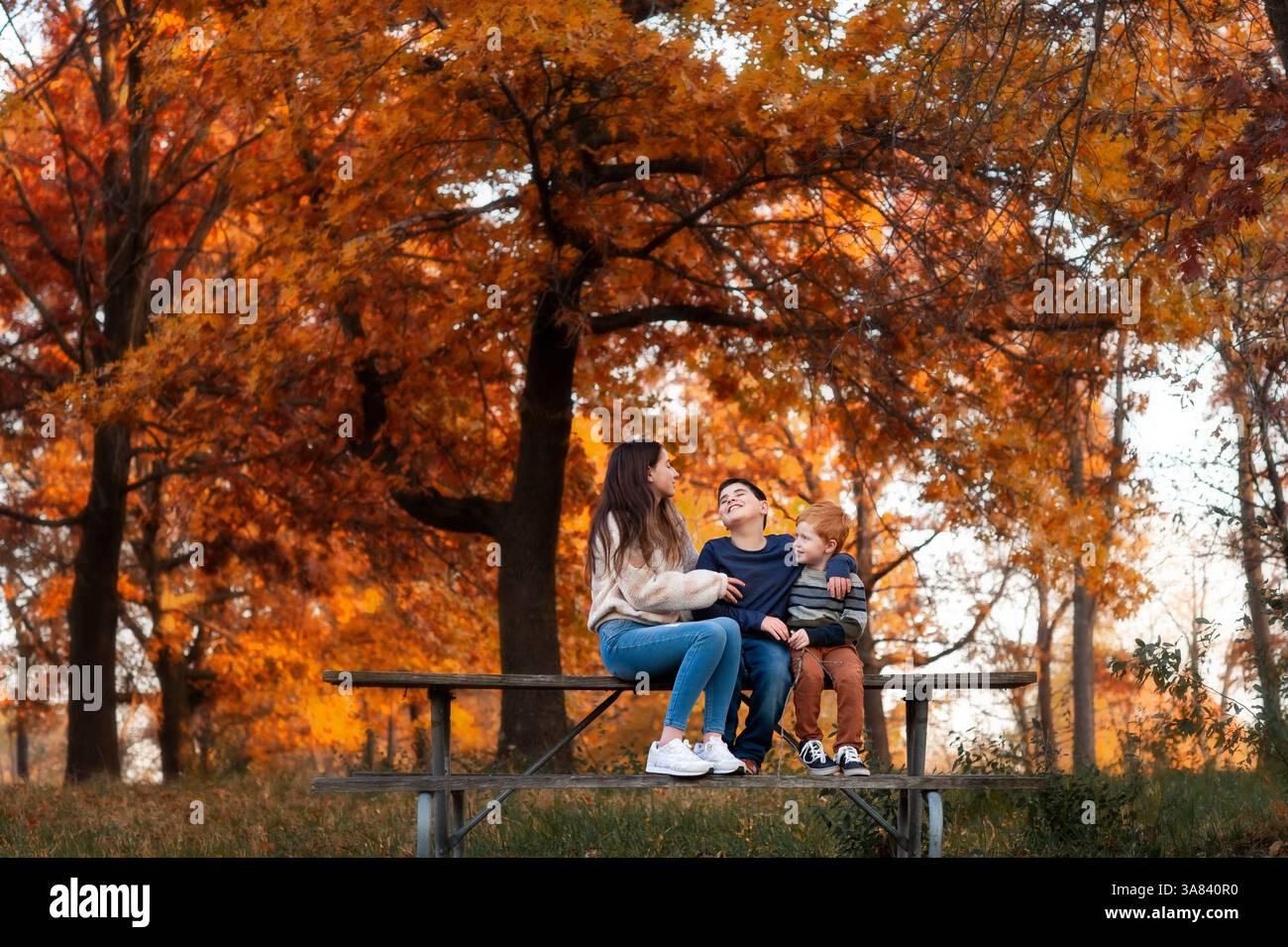 Drei Kinder sitzen zusammen und lachen im Herbst auf dem Picknicktisch im Park Stockfoto
