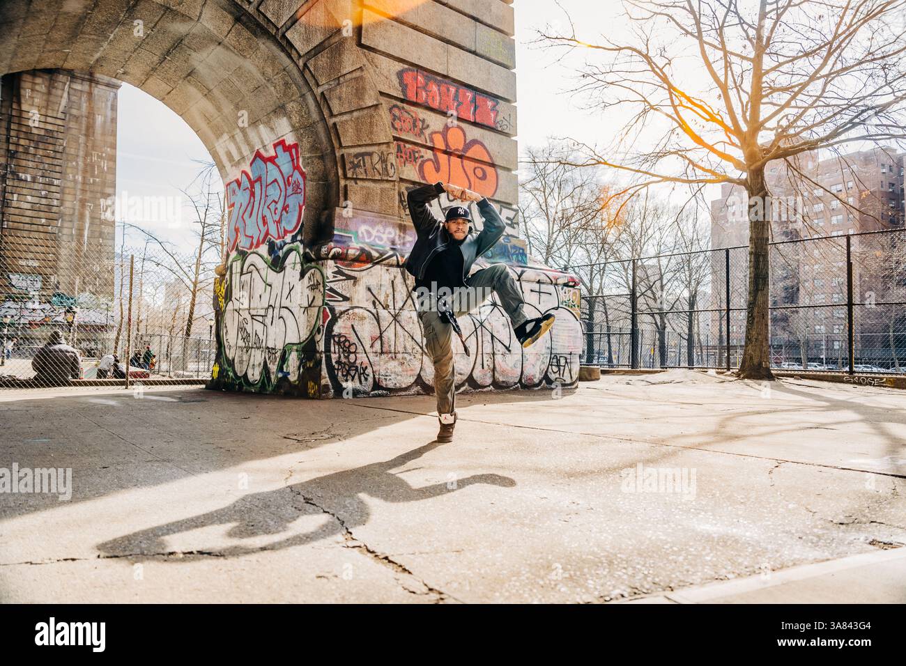 Straßentänzer mitten in der Luft unter Graffiti-bedecktem Bogen und Sonnenlicht Stockfoto