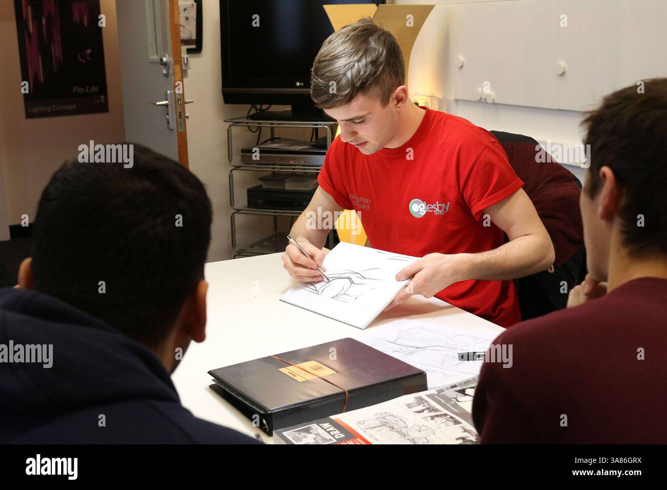 Ein junger Designlehrer demonstriert einer kleinen Gruppe von Designstudenten der Universität in einem Klassenzimmer das Skizzieren von Fahrzeugen Stockfoto
