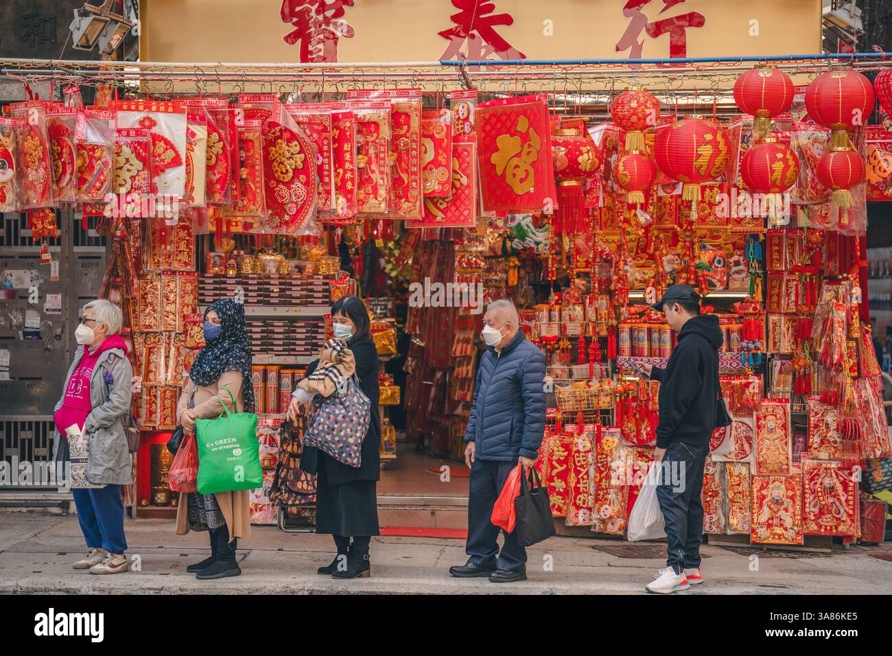 Die Leute warten an einer Bushaltestelle unter einer Laterne und einem Lei See Shop in Sheung Wan am chinesischen Neujahrsfest in Hongkong, China Stockfoto