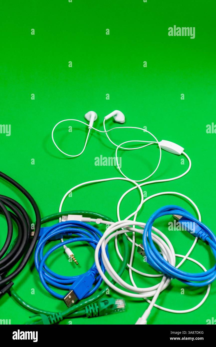 Kabelgebundene Kopfhörer und viele bunte Kabel auf grüner Oberfläche Stockfoto