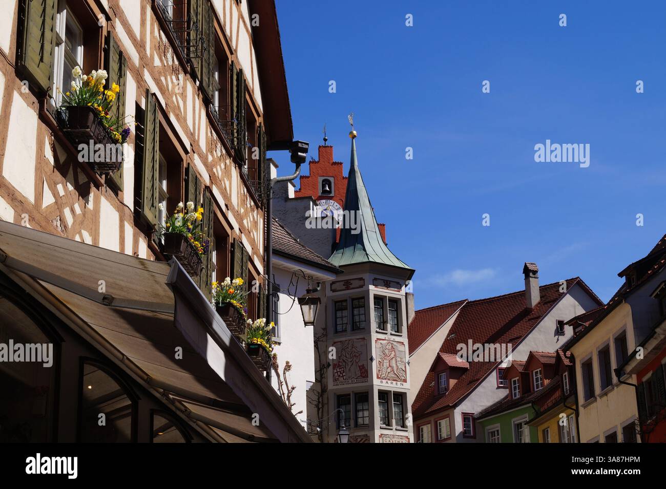 Charmantes Fachwerkhaus mit weißen und gelben Blumen an den Fenstern und anderen bunten alten Häusern in einer romantischen mittelalterlichen Stadt. April 2015 Stockfoto