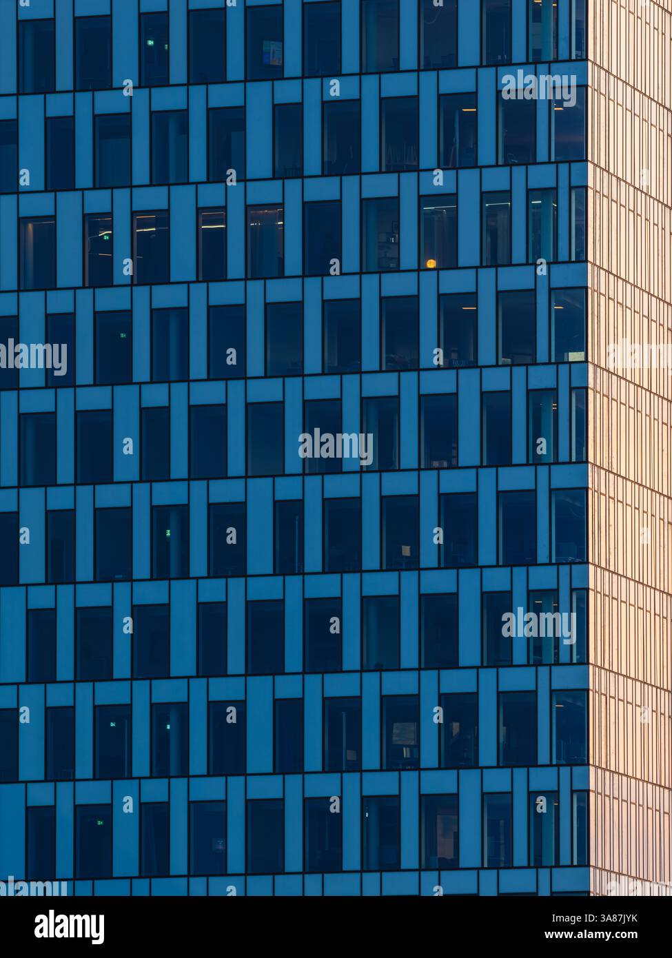 Die blau getönten Fenster eines Bürogebäudes in göteborg bilden ein Gittermuster. Ein Fenster leuchtet auf. Die Dämmerung sorgt für ein warmes Leuchten in der Ecke Stockfoto