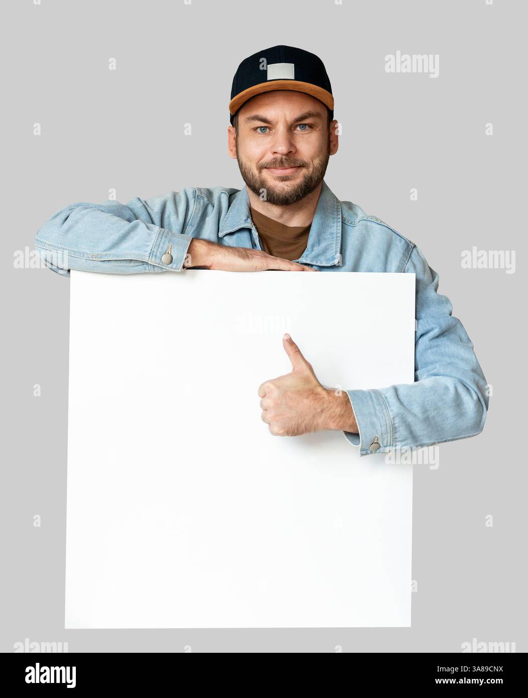Mann mit lässigem Outfit, der sich auf ein weißes Whiteboard stützt und die Daumen nach oben zeigt. Stockfoto