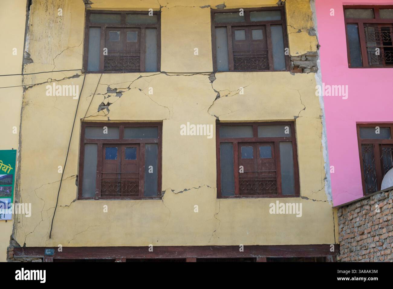 Eine gelbe Gebäudefassade weist erhebliche Risse auf, was auf strukturelle Schäden hindeutet, möglicherweise durch seismische Aktivität oder Absiedlungen. Stockfoto