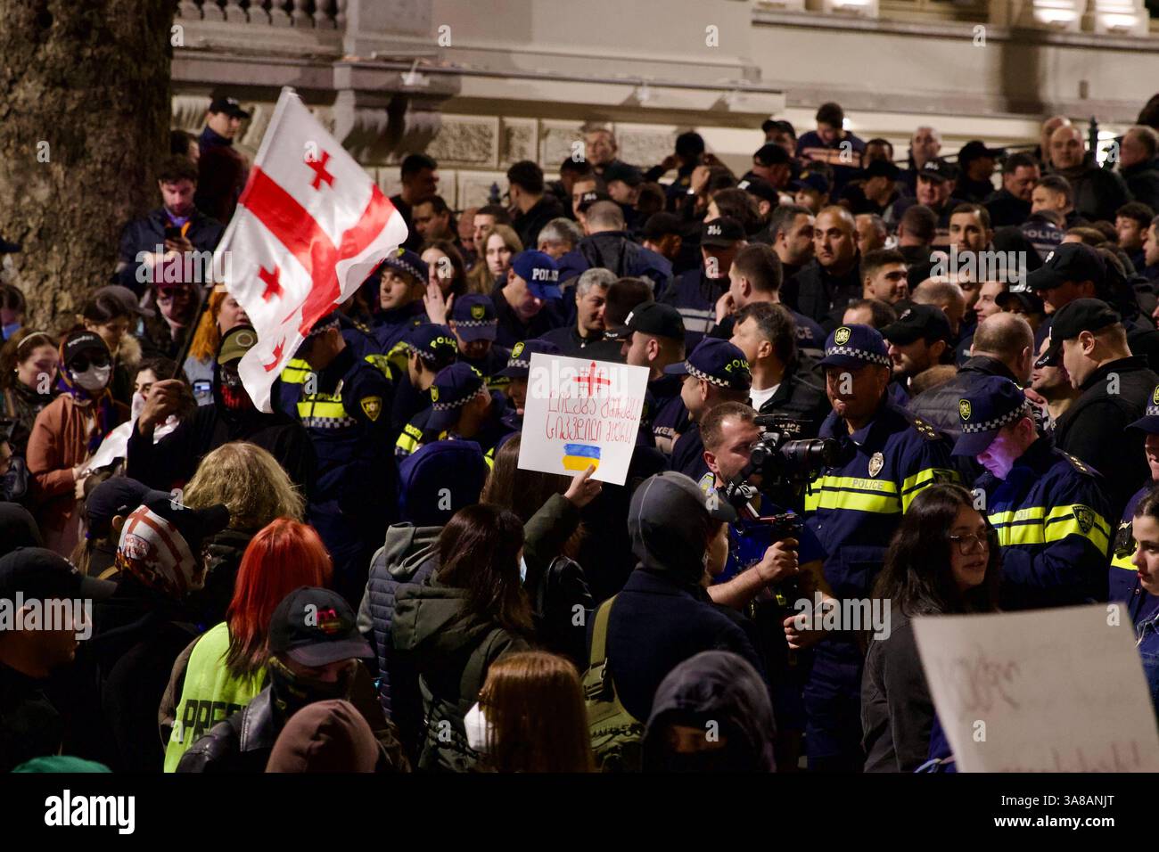 Ein Massenprotest in Georgien. Demonstranten mit Fahnen und Schildern stehen vor einer dichten Polizeikette. Stockfoto