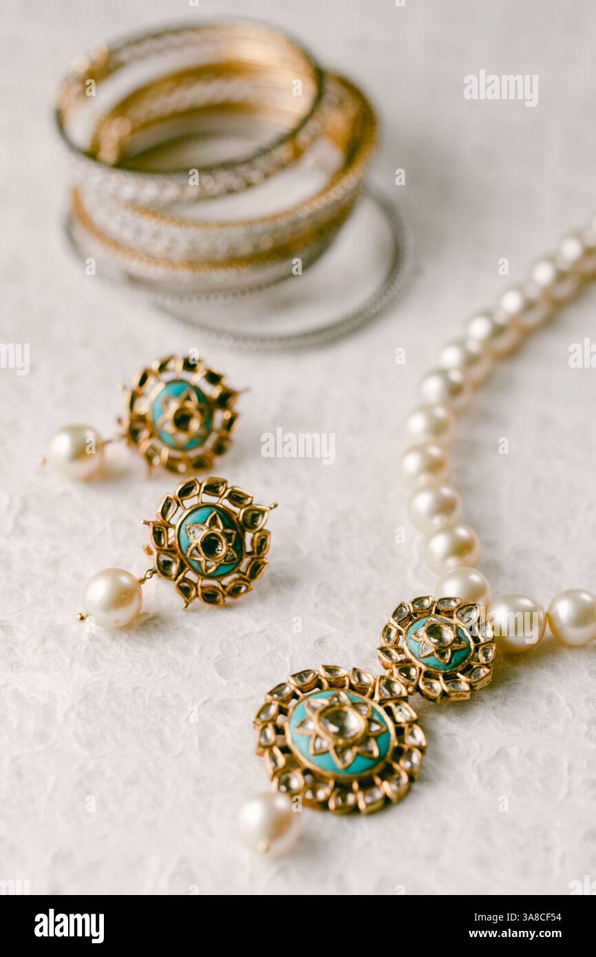 Zarte goldene Armreifen und eine Perlenkette mit komplizierten Details schaffen ein exquisites Schmuckarrangement. Stockfoto