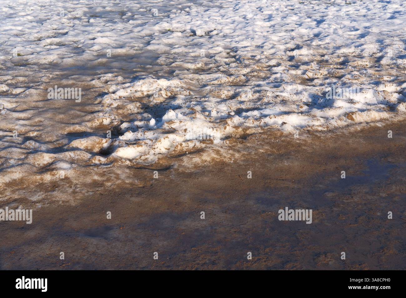 Schmutziger schmelzender Schnee mit nassem Sand im Spätwinter oder frühen Frühling. Wechselndes Wetter, Reinigung von Straßen, Parks und Straßen im Frühjahr. Kommunale Dienstleistungen Stockfoto