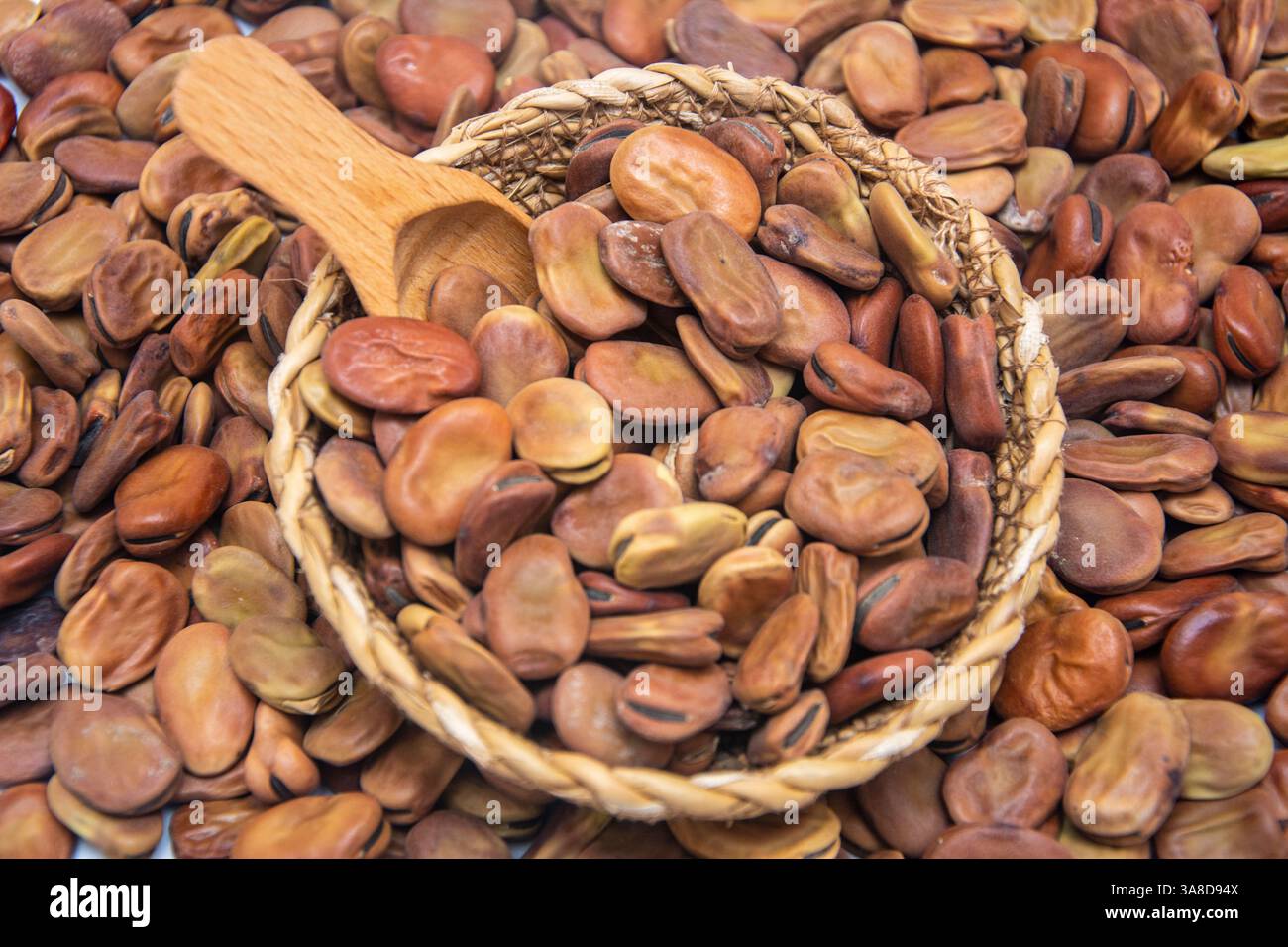 Eine Korbschale gefüllt mit breiten Bohnen mit einem Holzlöffel darin Stockfoto