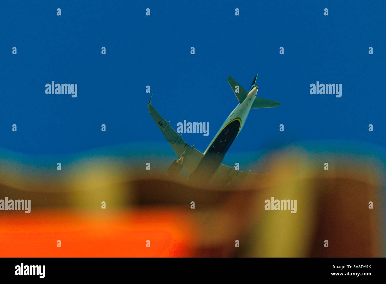 JETLINER FLIEGEN ÜBER DAS DACH EINES HAUSES IN GERINGER HÖHE, UNTER WOLKENLOSEM BLAUEM HIMMEL. Stockfoto