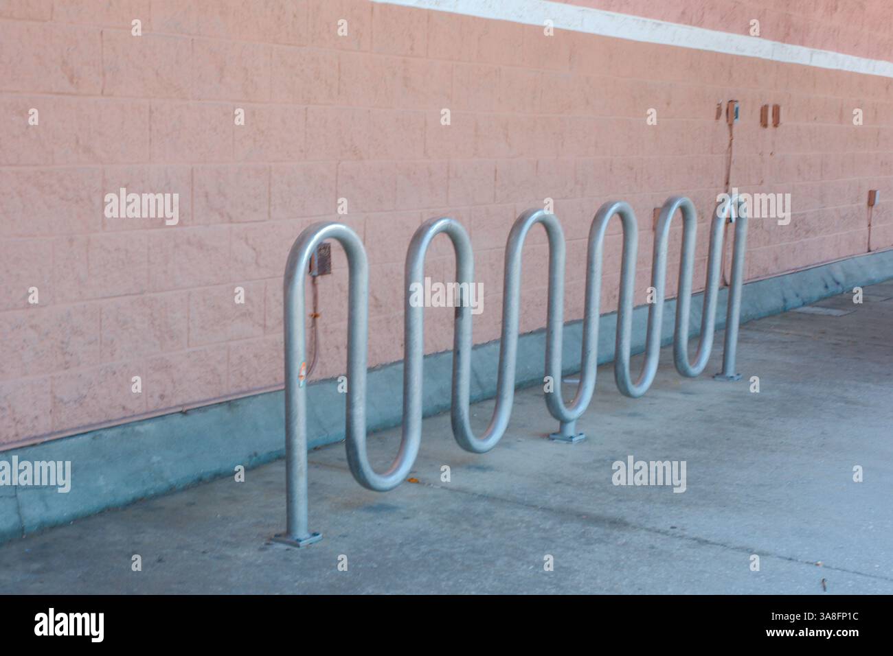 Serie von fünf silbernen, schleifenförmigen Fahrradträgern aus Metall, die in einer Reihe auf einer Betonoberfläche gegen eine hellrosa Ziegelwand montiert sind. Entwickelt zur Unterstützung von Bicyc Stockfoto