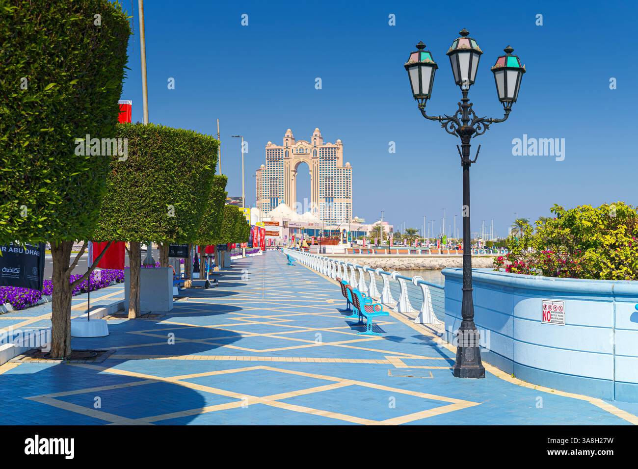 Abu Dhabi, Vereinigte Arabische Emirate - 10. Januar 2024, Panoramablick auf die Promenade mit Bäumen und Laternen, Rixos Marina Hotel im Hintergrund, tagsüber Stockfoto