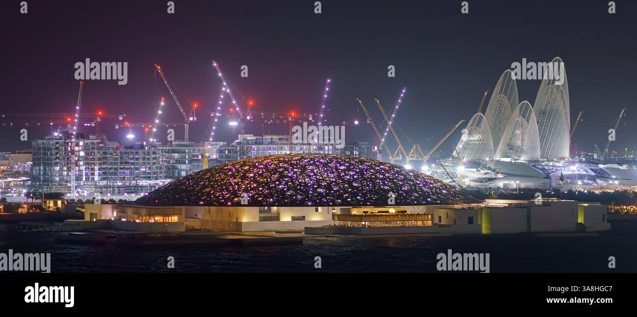 Abu Dhabi, Vereinigte Arabische Emirate - 17. Januar 2024, Blick auf das Meer aus der Luft auf den Louvre Abu Dhabi mit Gebäuden und Konstruktionen dahinter, nachts, mit Beleuchtung Stockfoto
