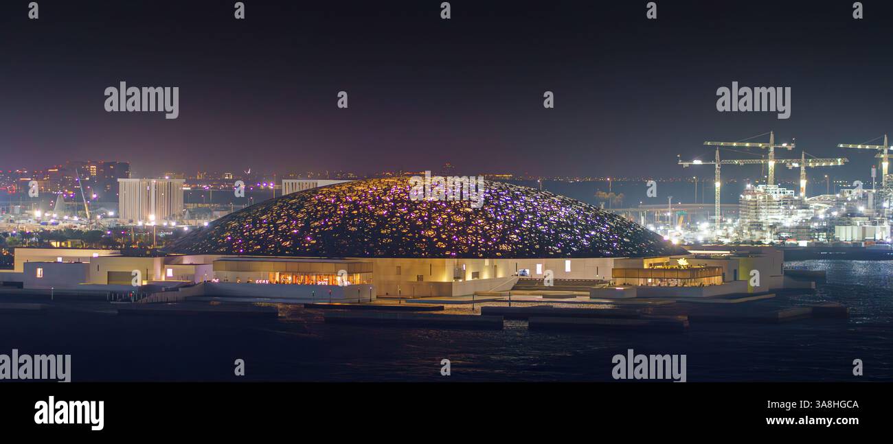 Abu Dhabi, Vereinigte Arabische Emirate - 17. Januar 2024, Blick auf das Meer aus der Luft auf den Louvre Abu Dhabi mit Gebäuden und Konstruktionen dahinter, nachts, mit Beleuchtung Stockfoto